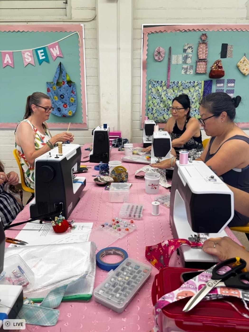 Three students working at sewing machines with the Hana Sew banner behind them